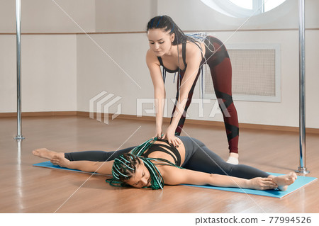 Pole dance studio, teacher helps athlete to do exercise. Pole dance studio, teacher helps athlete to do exercise. 77994526