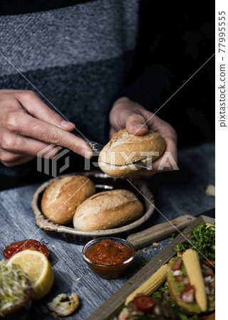 man cuts a bread bun to prepare a sandwich man cuts a bread bun to prepare a sandwich 77995555