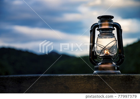 An oil lantern that burns with a soft flame on the shore of a lake 77997379
