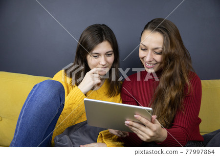 young lesbian couple hold tablet chatting and messaging on sofa young lesbian couple hold tablet chatting and messaging on sofa 77997864