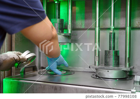 Steel Manufacturing Plant. A Worker is Placing a Piece of Metal Inside the Press. The Press is Steel Manufacturing Plant. A Worker is Placing a Piece of Metal Inside the Press. The Press is 77998108