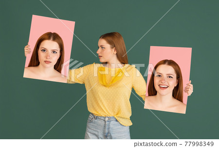 Young red headed girl holding her portraits isolated over green studio background with copyspace for ad. Concept of beauty, fashion. 77998349