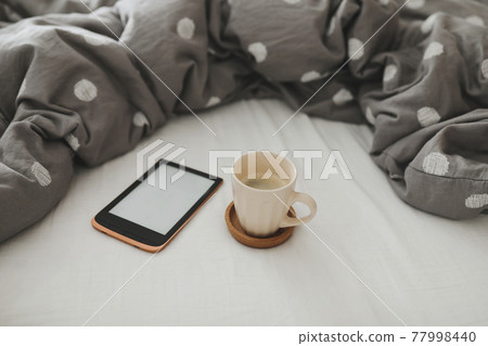 E-book and a cup of coffee in bed on the sheets. Good morning. Breakfast in bed E-book and a cup of coffee in bed on the sheets. Good morning. Breakfast in bed 77998440