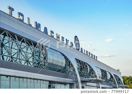 Novosibirsk, Russia, 19.07.2018: A sign on the Tolmachevo Airport building, outside view of the glass windows of the building from the visitors entrance Novosibirsk, Russia, 19.07.2018: A sign on the Tolmachevo Airport building, outside view of the glass windows of the building from the visitors entrance 77999317
