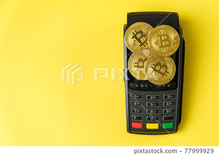Bitcoin coins on the payment terminal on the yellow background. Bitcoin coins on the payment terminal on the yellow background. 77999929