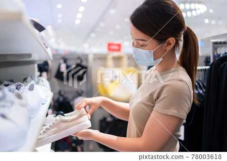 Asian woman wearing face mask choosing sneaker discount sale while coronavirus pandemic in store Asian woman wearing face mask choosing sneaker discount sale while coronavirus pandemic in store 78003618