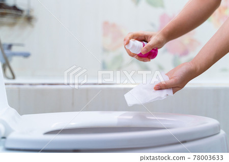 close up hand cleaning Toilet seat by a wet wipe with alcohol spray in public restroom for coronavirus prevention and hygiene before using 78003633