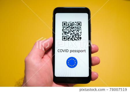 A smartphone with electronic immune digital health passport, Covid pass with QR code in mans hand on the yellow background. 78007519