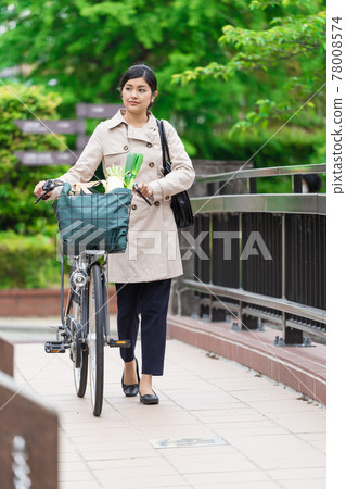 A young woman walking while pulling a shopping bag in a bicycle basket A young woman walking while pulling a shopping bag in a bicycle basket 78008574