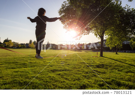 Adventurous White Caucasian Adult Woman walking on a Slackline 78013121