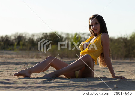 Confident young sensual lady resting on sandy seashore in sunlight 78014649
