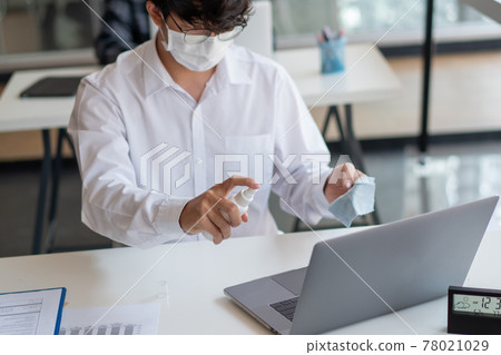 Covid-19 concept a businessman cleaning his laptop to prevent Coronavirus outbreak (COVID-19) by using alcohol spray at his workplace 78021029
