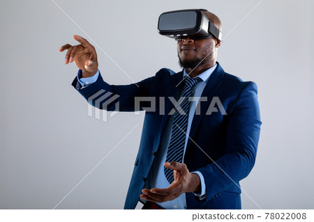 African american businessman wearing vr headset gesturing against grey background 78022008