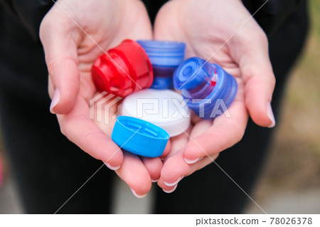 Closeup at caucasian female hands full of colorful plastic bottle cups, handful of waste of plastic lids. Recycling. Collecting bottle caps 78026378