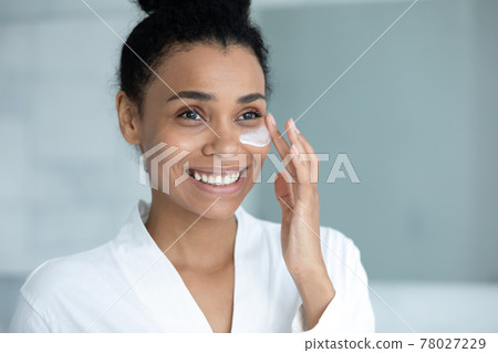 Smiling Afro American woman in bathrobe spreading moisturizing collagen cream 78027229