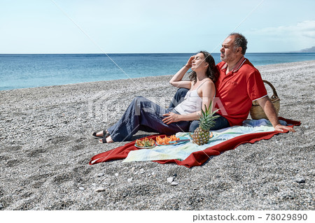 Middle aged couple having a picnic at the seaside with fresh exotic fruit. Spring, summer time lifestyle, love dating concept. 78029890