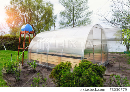 DIY wooden base with elevated water storage tank for autonomous drip irrigation of garden bed and growing green fresh organic vegetable in eco-friendly small greenhouse yard. Domestic farming concept 78030779