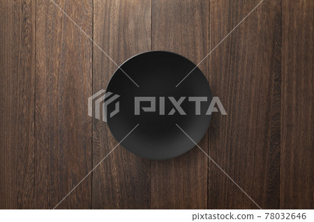 A black round plate on a natural wood table [a bird's-eye view] 78032646