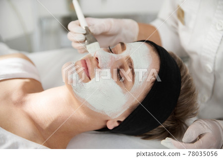 Closeup of cosmetologist applying an alginic mask on a beautiful woman face 78035056