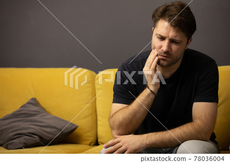 unshaven guy sits on sofa and suffers from toothache. dentist help, dental care unshaven guy sits on sofa and suffers from toothache. dentist help, dental care 78036004