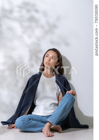 A young woman leaning against a white wall in the sunlight through the trees 78038090