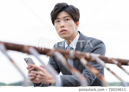 A young businessman twilight with a smartphone on the roof 78039611