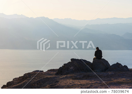 A man sits on a high mountain cliff and overlooks the horizon. A concept for hope, peace, power, soul searching 78039674
