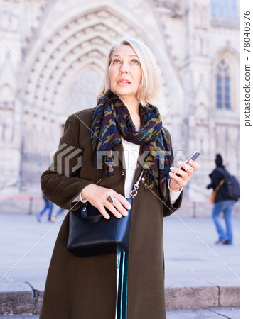 Smiling mature female is walking and talking by phone Smiling mature female is walking and talking by phone 78040376