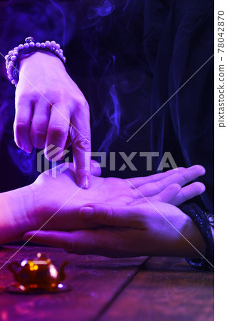 Witch is a fortune teller reading good luck close-up. Fortune teller guides the lines on the client's hand in neon light 78042870