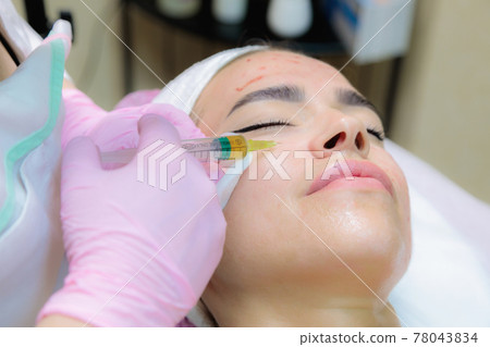 The doctor gives injections of blood plasma into the face of a young girl. 78043834