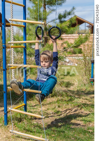 A blonde-haired child is playing on the playground, hanging on rings A blonde-haired child is playing on the playground, hanging on rings 78043840