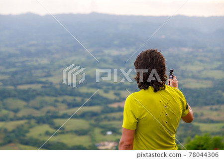 A long-haired man filming a video with a small video camera, a picturesque valley 78044306