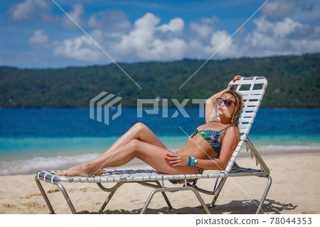 A young beautiful girl sunbathes on a sun lounger by the ocean. 78044353