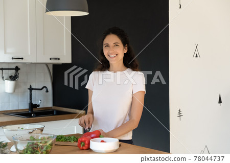 Happy beautiful young housewife cooking food in kitchen. 78044737