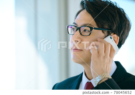A young businessman in a suit calling on his smartphone in the office corridor 78045652