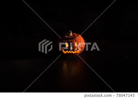 Halloween, orange pumpkin with a scary luminous face on a dark background. Thick gray smoke comes out and spreads across the black table. A close-up of a flashlight . Decorated candle stand. 78047143