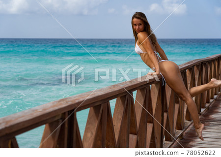 Beautiful woman posing on a pier with blue water in a white bikini. Vacation and travel concept. 78052622