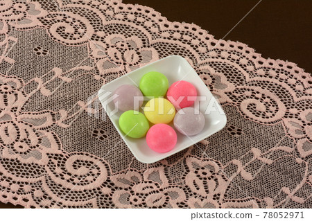 Multicolor soda pop mint candies small white candy dish on pink lace table runner on brown tablecloth Multicolor soda pop mint candies small white candy dish on pink lace table runner on brown tablecloth 78052971