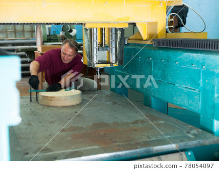 Concentrated worker installs wooden blank in CNC machine Concentrated worker installs wooden blank in CNC machine 78054097