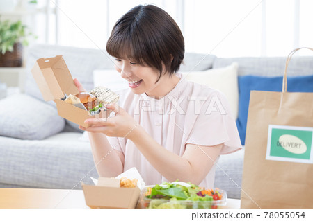A woman eating the food ordered by delivery A woman eating the food ordered by delivery 78055054