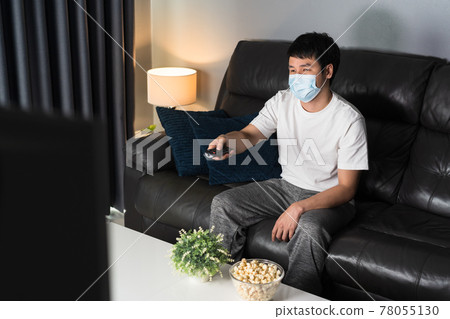 man watching TV on sofa and wearing medical mask to protect coronavirus (Covid-19) man watching TV on sofa and wearing medical mask to protect coronavirus (Covid-19) 78055130