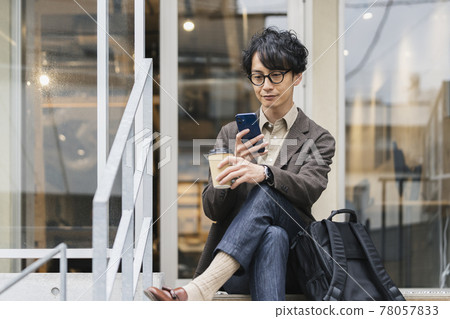 一個三十出頭的男人，戴著眼鏡，外賣杯和智能手機 78057833