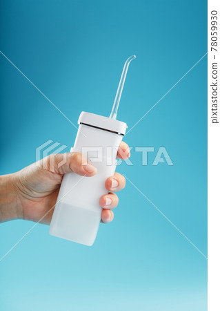 White irrigator in hand for cleaning teeth on a blue background. 78059930