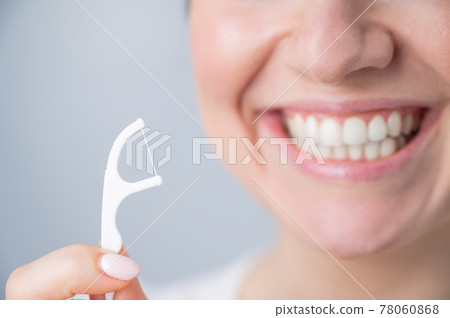 Close-up portrait of a beautiful caucasian woman with a flawless smile holding a toothpick with dental floss on a white background 78060868