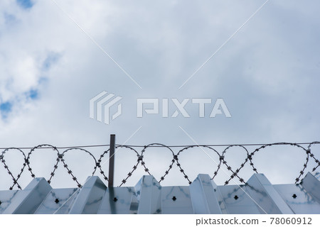 High metal corrugated wall with barbed wire and gray sky High metal corrugated wall with barbed wire and gray sky 78060912