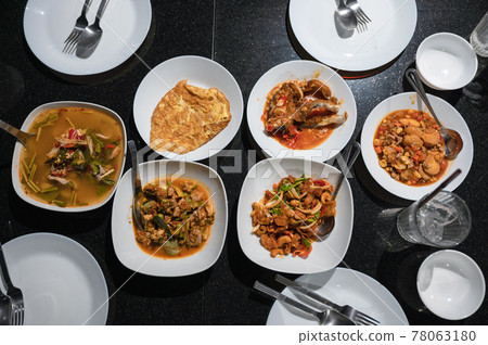 Variety of Thai food with spicy soup, fried fish, tofu, chicken curry, salad and silverware on dining table at dinner Variety of Thai food with spicy soup, fried fish, tofu, chicken curry, salad and silverware on dining table at dinner 78063180