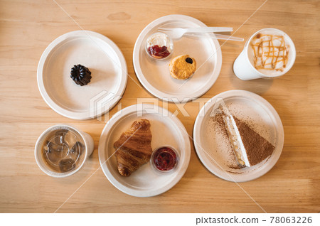 Croissant, Banoffee, Scone, Canele on paper plate and iced coffee on wooden table in the cafe Croissant, Banoffee, Scone, Canele on paper plate and iced coffee on wooden table in the cafe 78063226