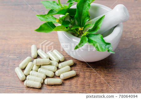 Pile of herbal medicine in capsules and ceramic mortar with green leaf. Pile of herbal medicine in capsules and ceramic mortar with green leaf. 78064094