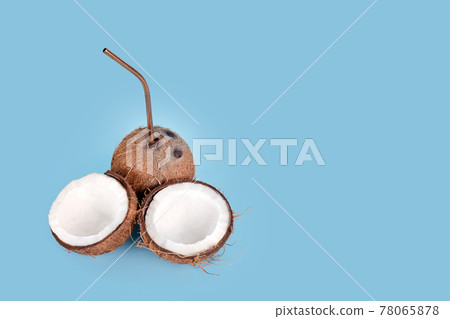 Open coconut with straw on blue background. Tropical drink, summer vacation minimal creative concept. Cracked coconut fruit with coconut milk inside, copy space for text 78065878