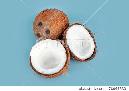 Whole and cracked coconuts on light blue background. De-husked coconut fruits showing the characteristic three pores. Cut in half coconut closeup. 78065880